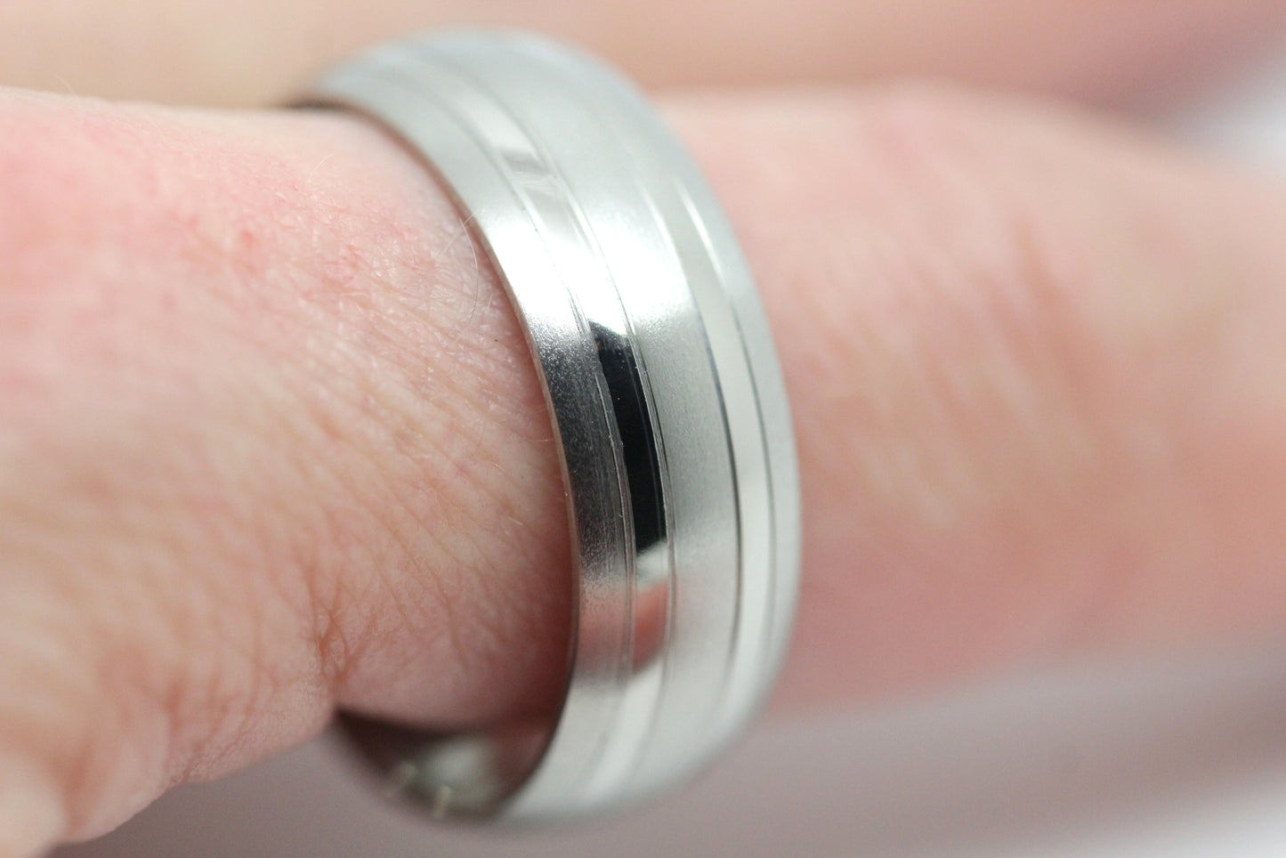 Close-up of a matte titanium wedding band with polished lines being worn on the finger, showcasing its design.