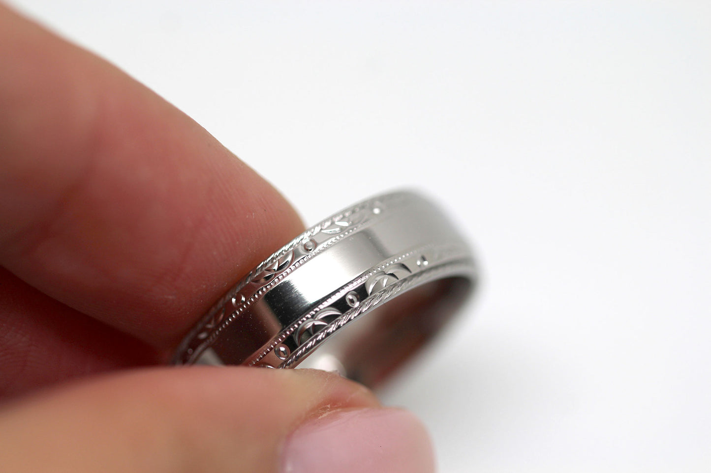 Close-up of a polished titanium wedding ring with filigree edge being held, showcasing its design.