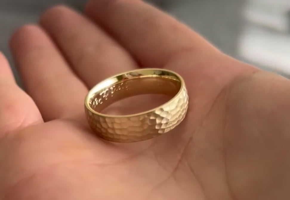 Gold ring with a hammered design held in a hand.
