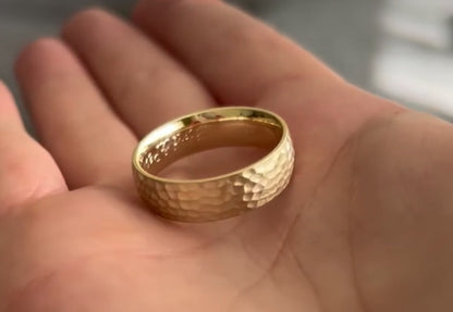 Gold ring with a hammered design held in a hand.